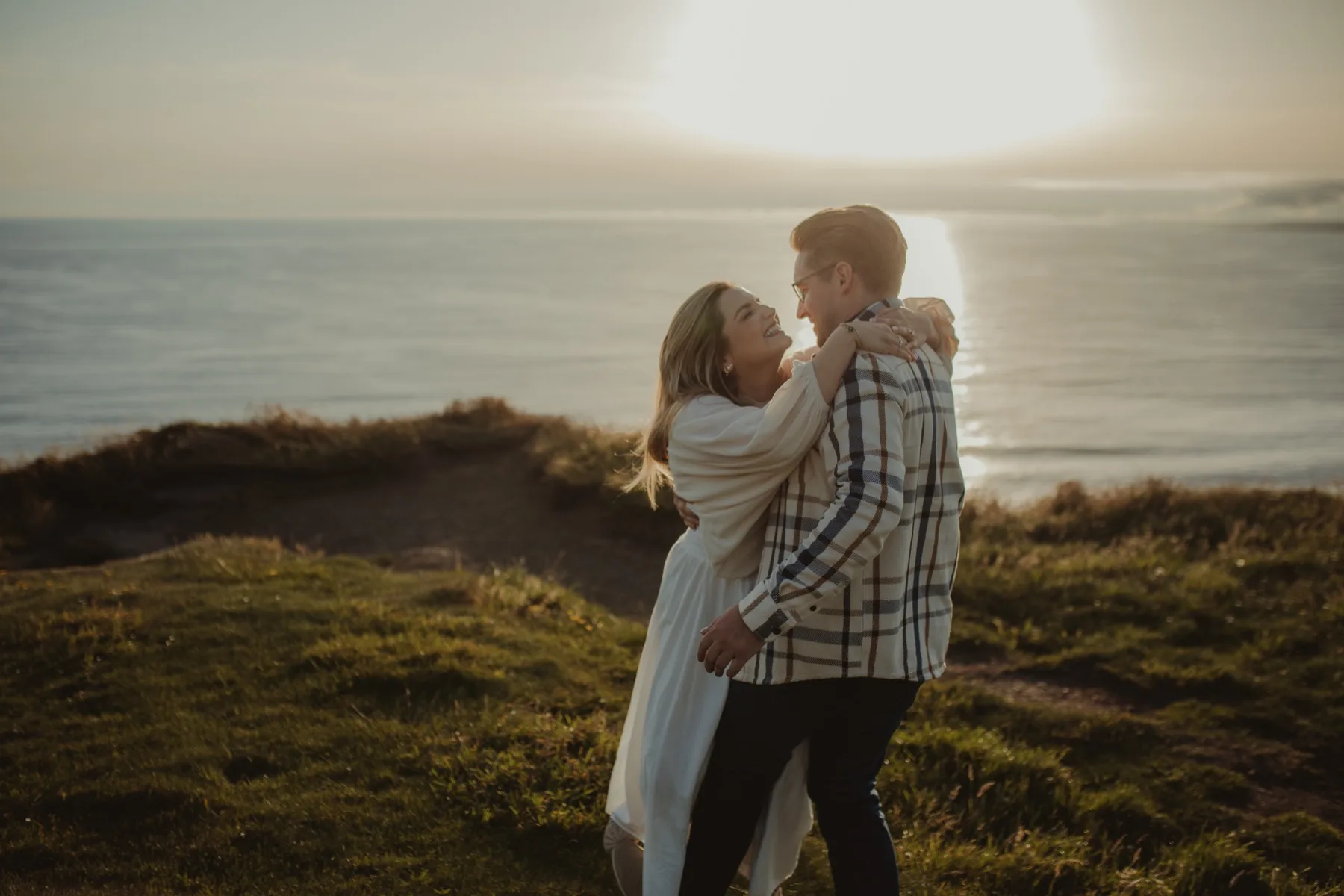 Shannon and Oscar embracing in front of a low sun over the sea.