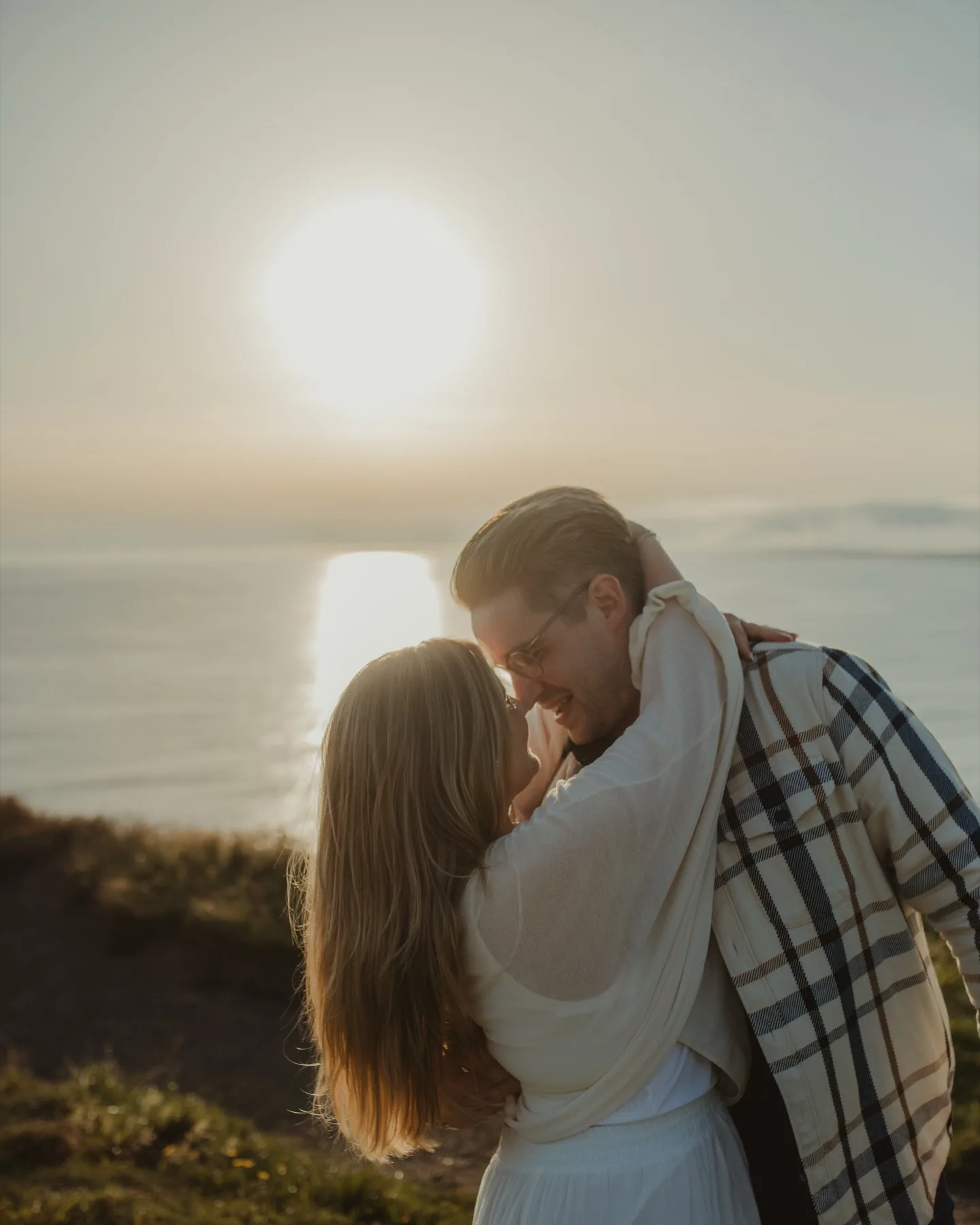 Shannon and Oscar embracing in front of a low sun over the sea.